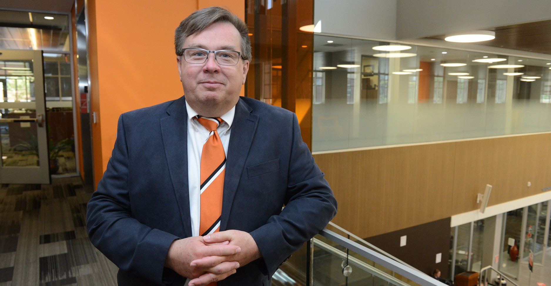 headshot of gray haired man in blue suit and orange tie