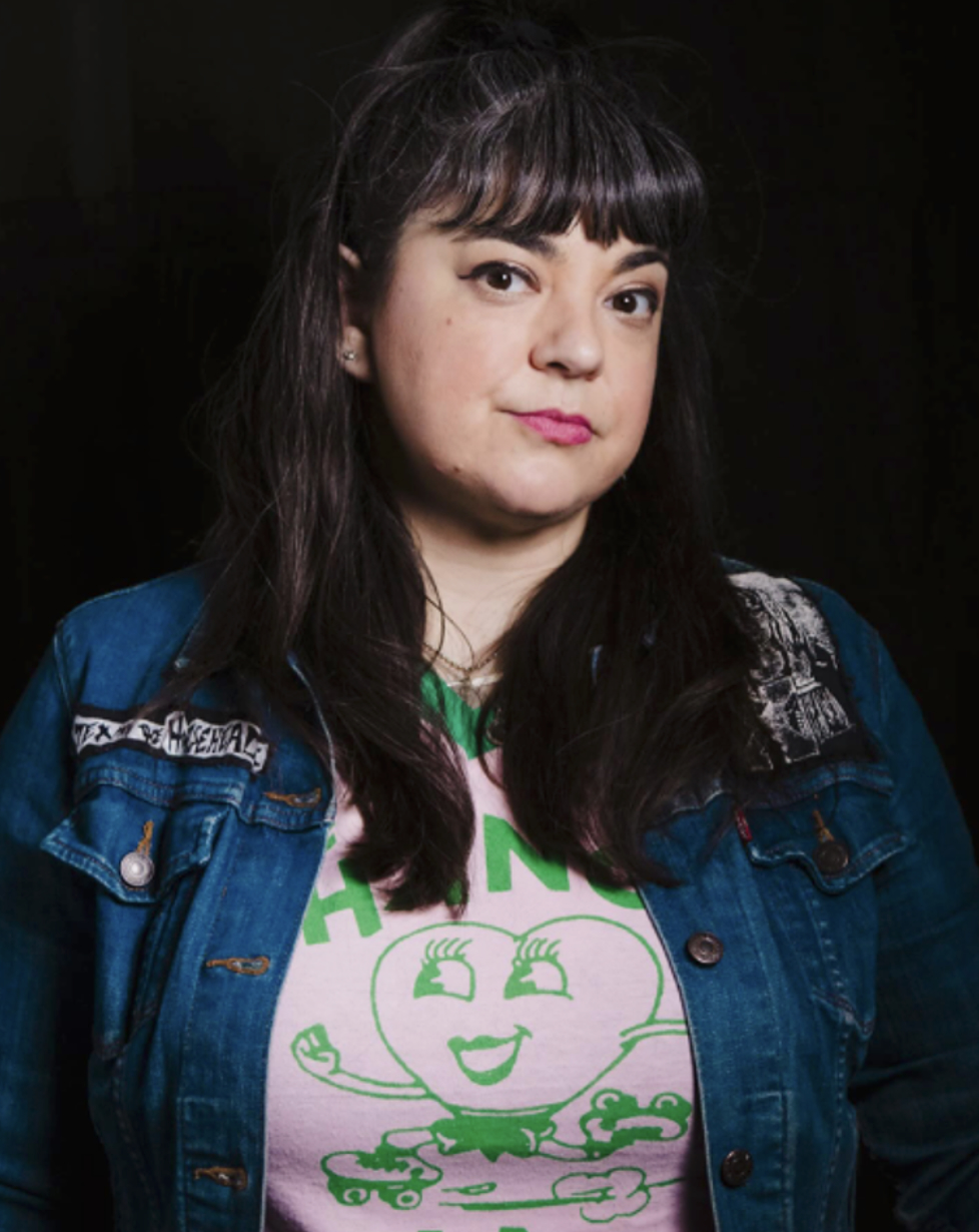 Headshot of dark haired woman in pink graphic tee and jean jacket.